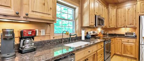 A kitchen with wooden cabinets, a granite countertop, a dishwasher, a microwave, a toaster, and a window with a view of greenery.