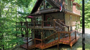 Eine mehrstöckige Holzhütte mit einer Terrasse und Treppe, umgeben von Bäumen.