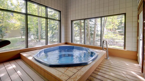 Un jacuzzi en una habitación con ventanas amplias, suelo de madera y vistas a árboles.