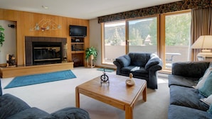 Una sala de estar con chimenea, televisor y un ventanal con vista a árboles.