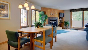 Una sala de estar moderna con una mesa de comedor de madera, sillas tapizadas en verde, una chimenea y ventanas amplias.
