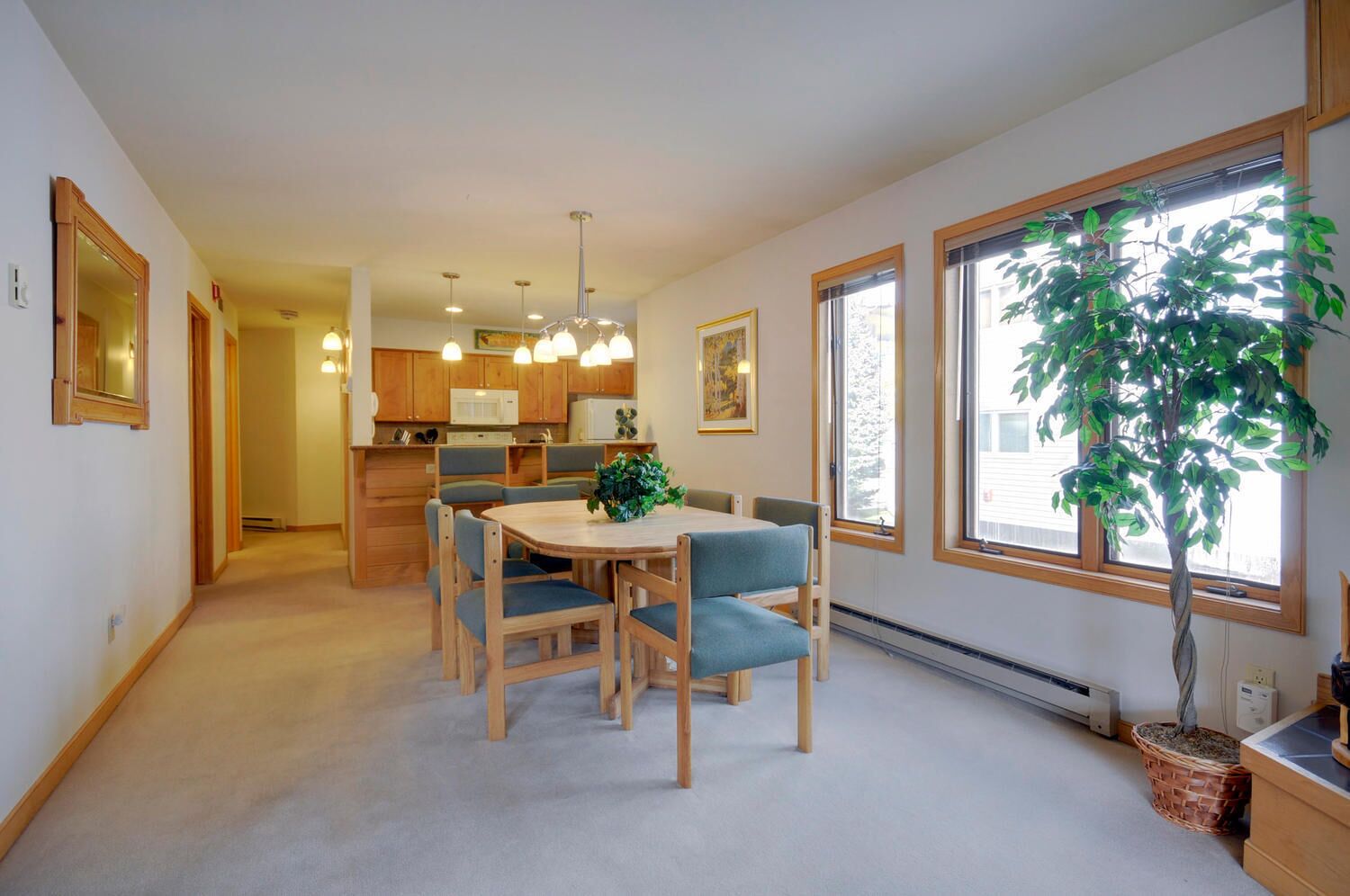 Une cuisine moderne avec des meubles en bois, une table à manger avec des chaises, des luminaires suspendus et une grande fenêtre donnant sur l’extérieur.