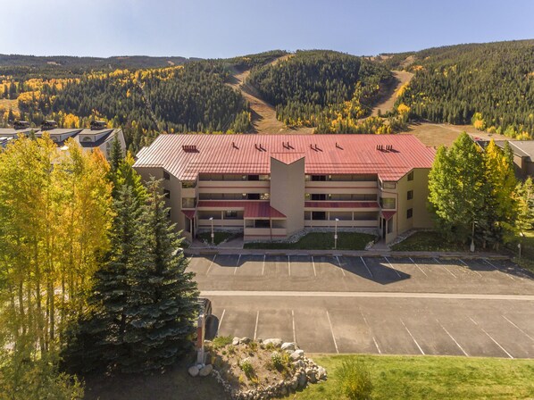 A multi-story hotel with a red roof, a parking lot, and a mountainous backdrop. - Ski Run Condo with Ski Run Views off deck, 3min walk to base, private entrance (Keystone)