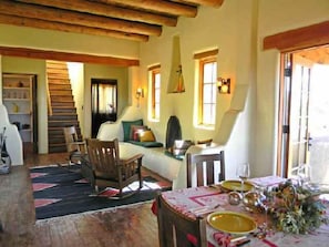 Uma sala de estar aconchegante com sofá, cadeiras, uma mesa de jantar posta com pratos e copos, e uma escada que leva a outro andar.