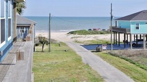 Une propriété située en bord de mer, offrant une vue sur la plage, dotée d’une terrasse en bois et d’un petit espace de stationnement.