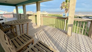 Une terrasse en bois avec une table et des chaises, donnant sur une plage et l’océan.
