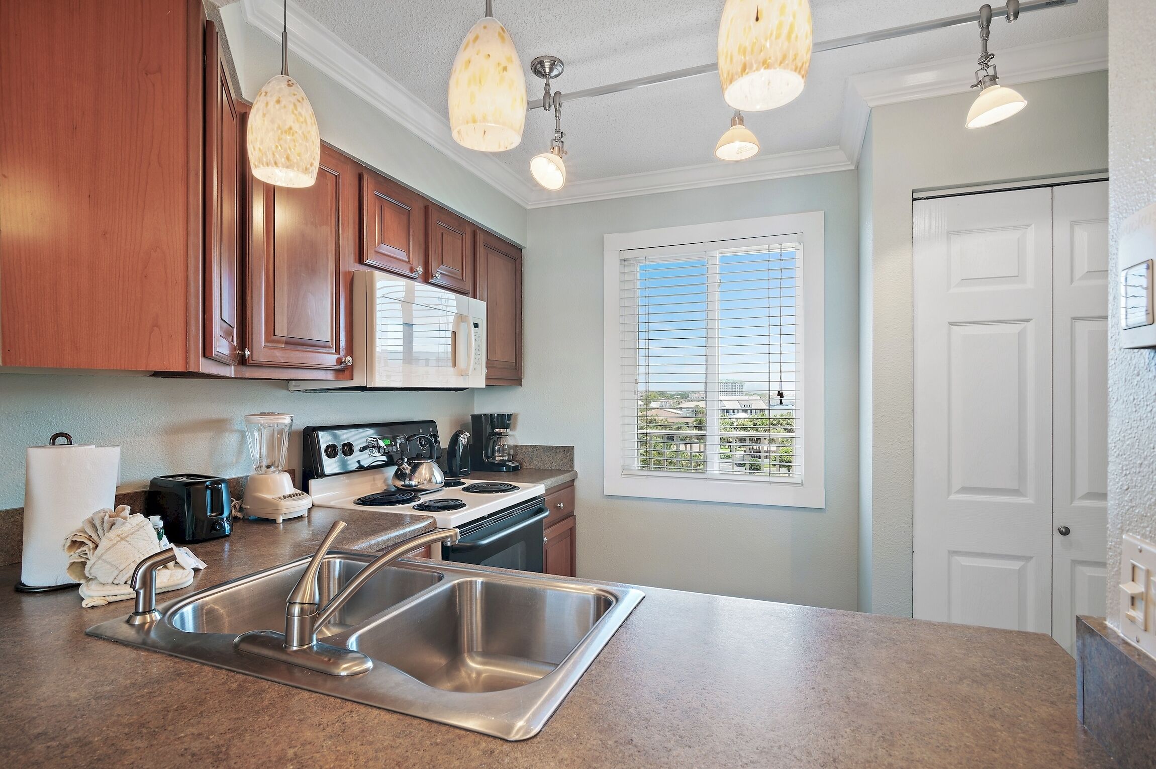 A kitchen with wooden cabinets, a stainless steel sink, and a window with blinds.