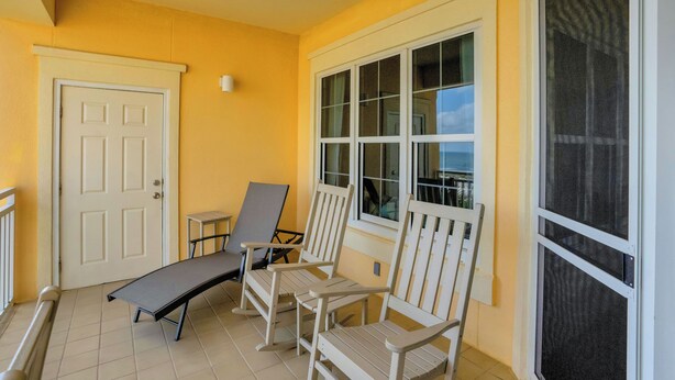 Een balkon met een witte deur, twee schommelstoelen, een klein tafeltje en uitzicht op de oceaan.