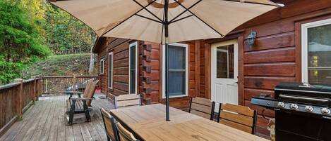 A wooden deck with a table and chairs, a barbecue grill, and a large umbrella.