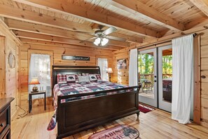 A cabin-style bedroom with a wooden ceiling, a bed with a quilt, a ceiling fan, and a view of the outdoors through a sliding glass door. - Falling Waters - hot tub, game table, views! (Banner Elk)