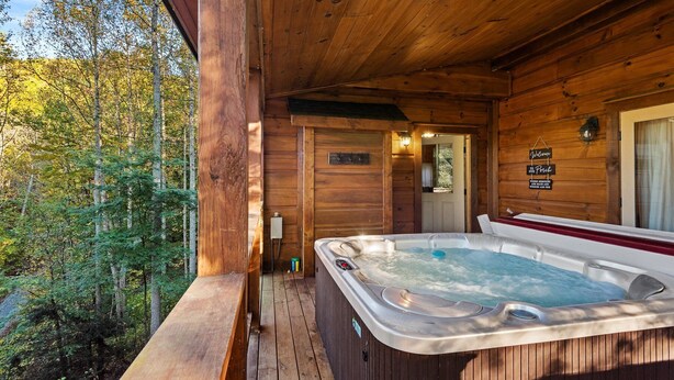 Una cabaña de madera con jacuzzi en una terraza de madera, rodeada de árboles.