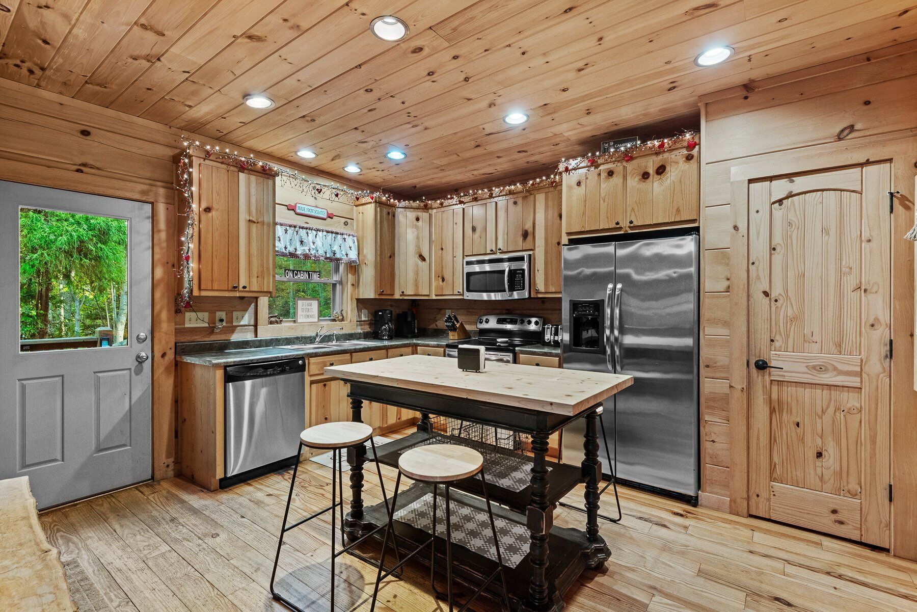 A cabin-style kitchen with wooden cabinets, a stainless steel refrigerator, and a wooden dining table with stools.