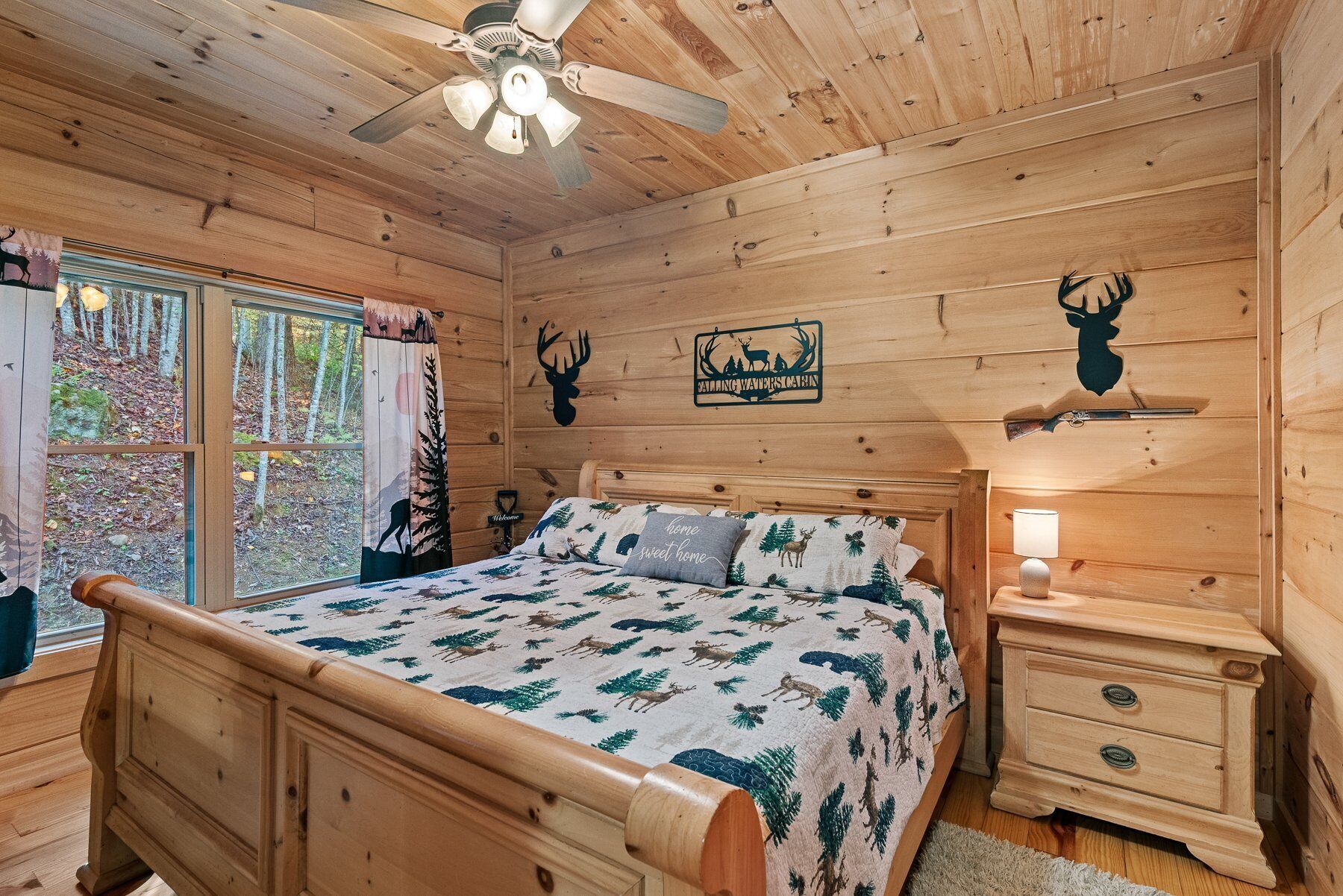 A wooden cabin bedroom with a bed, nightstands, a ceiling fan, and a window with curtains.