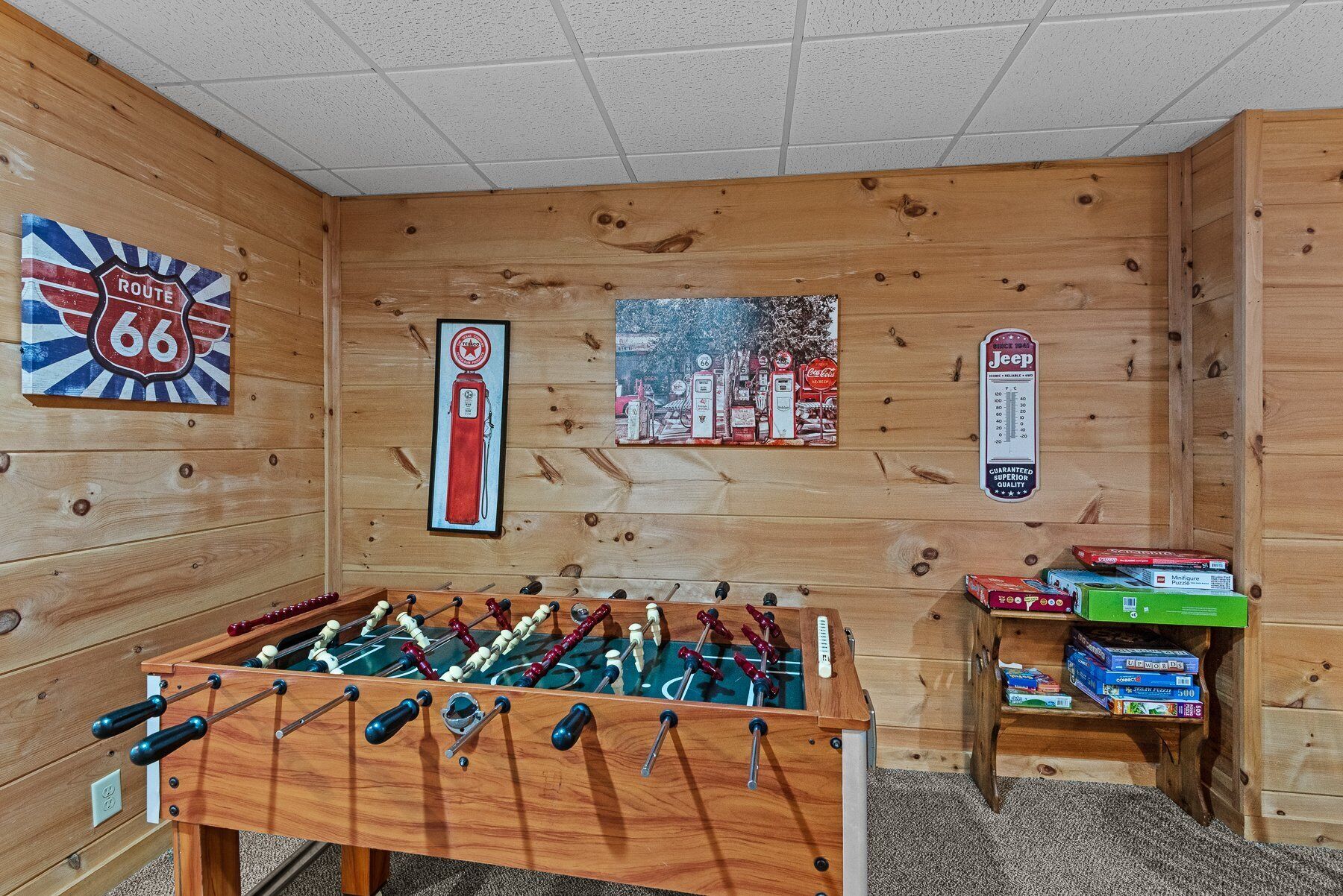 Una habitación con mesa de fútbolín, pared decorada con ilustraciones de la Ruta 66 y gasolineras, y estante con juegos de mesa.