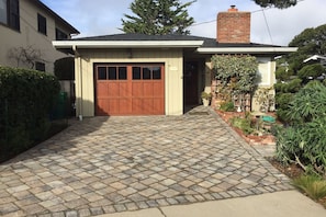 A residential house with a brick chimney, a garage with a wooden door, and a paved driveway. - Boathouse - Pacific Grove House - Walk to the Water (Pacific Grove)