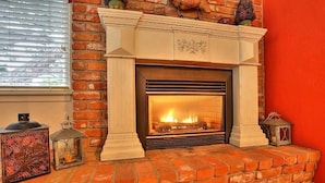 Une cheminée avec un feu, entourée d’un mur en briques et surmontée d’un manteau de cheminée blanc.