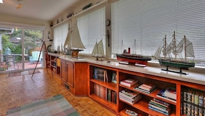 Une pièce avec un plancher en bois, une bibliothèque remplie de livres et une fenêtre avec des stores.