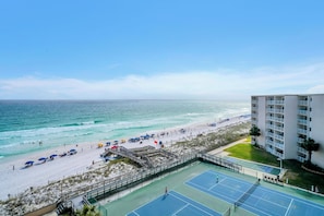 A beach view with a tennis court, a beach umbrella area, and a building with balconies. - 720 -Breathtaking Sunset Views, Walk-in Shower, FREE beach service (Destin)
