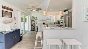 A modern kitchen with a central island, white bar stools, and pendant lighting.