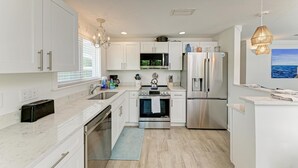 A modern kitchen with white cabinetry, stainless steel appliances, and a view of the ocean through a window.