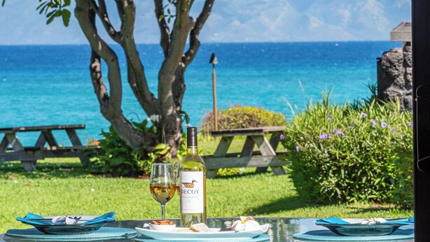 Un tavolo apparecchiato con bottiglia di vino, bicchieri e cibo, con vista su una spiaggia e l'oceano.