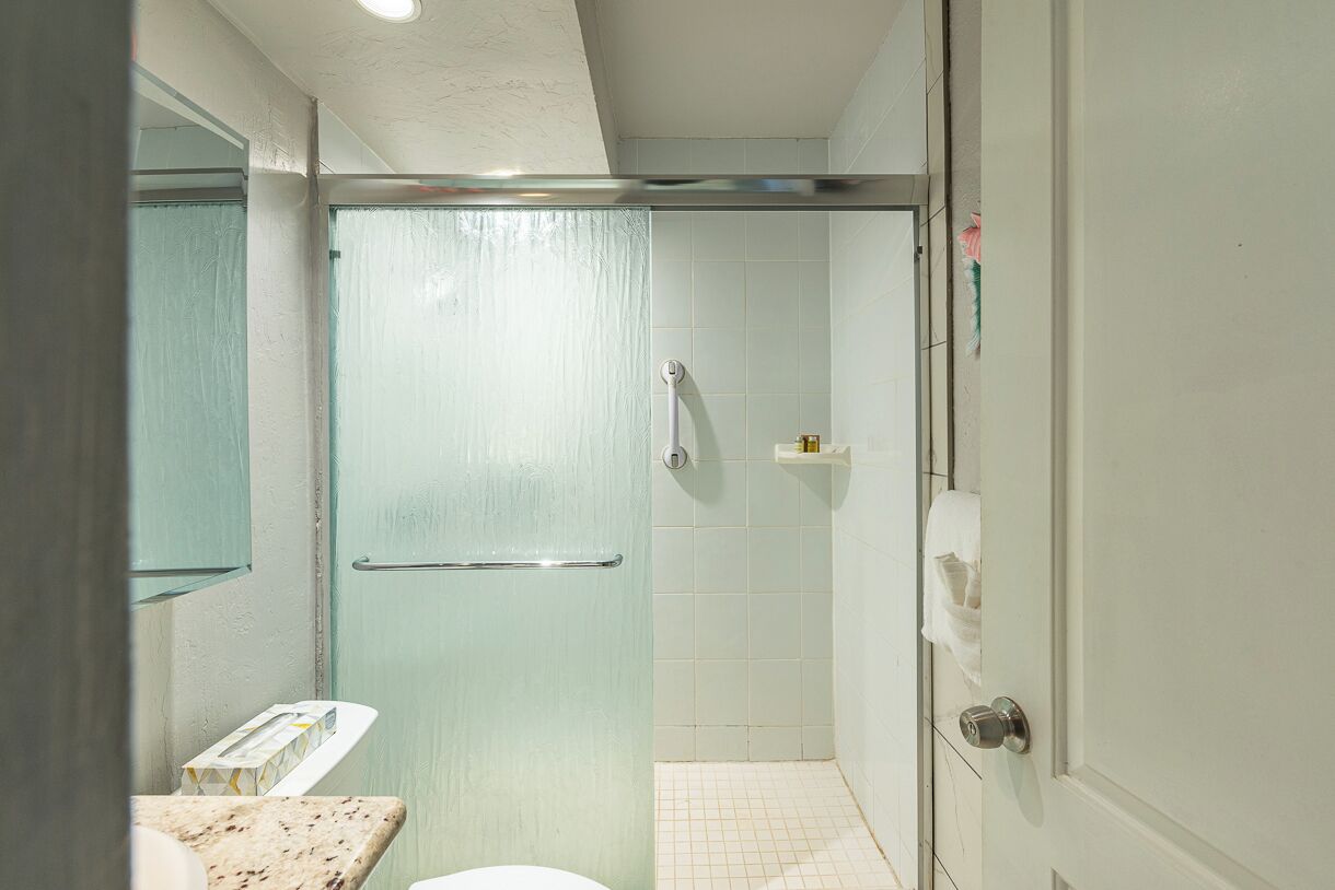 Une salle de bain avec une porte de douche en verre, des toilettes et un lavabo doté d’un plan de travail en marbre.
