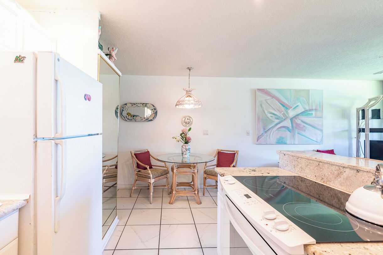 Een kleine keuken met een eettafel, stoelen, een koelkast en een fornuis.