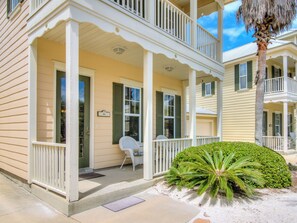 A two-story building with a porch, a covered outdoor seating area, and a small palm tree.