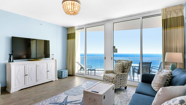 A modern living room with a large TV, a sofa, a coffee table, and a balcony with a view of the sea.