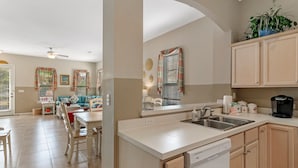 A modern kitchen with a dishwasher, a coffee maker, and a sink. There is a dining area with a table and chairs. - Alabama Sunrise- 3BR/3BA crescent beach home - Pet Friendly (Gulf Shores)