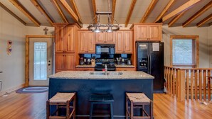 A spacious kitchen with wooden cabinets, a large island with stools, a black refrigerator, and a wooden ceiling with exposed beams.