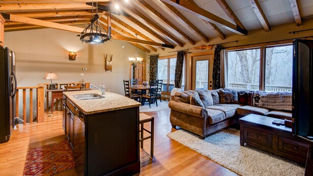 A spacious living area with a wooden ceiling, a kitchen with a granite countertop, and a cozy seating area with a sofa and a coffee table.