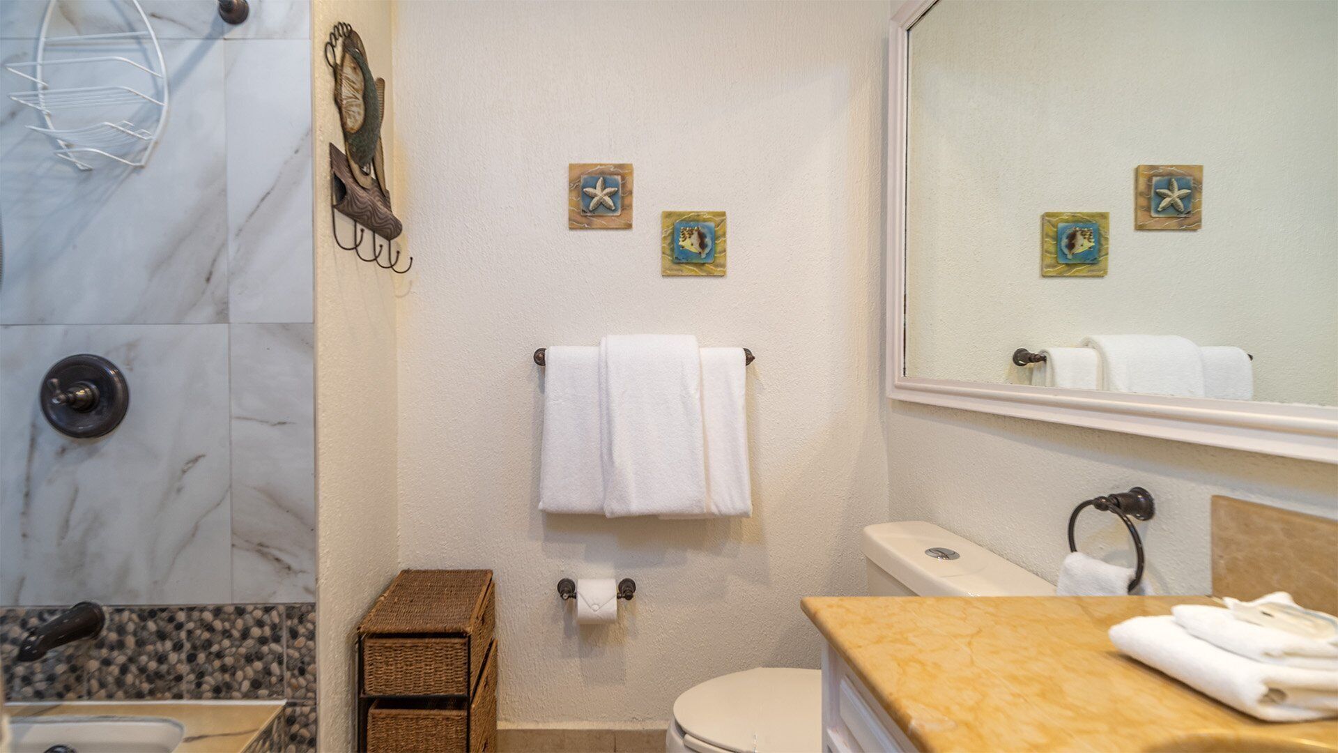 Baño con ducha de mármol, inodoro, lavabo y espejo. Se observan dos adornos de estrella de mar en la pared.