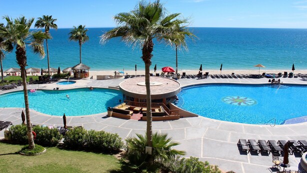 A resort pool area with multiple swimming pools, lounge chairs, and palm trees.