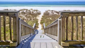 Una pasarela de madera que conduce a una playa con aguas azul cristalino y arena blanca.