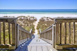 A wooden boardwalk leading to a beach with clear blue water and white sand.