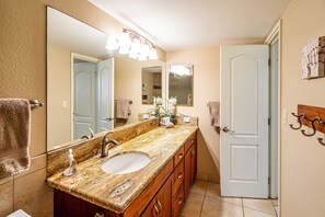 Un baño con lavamanos de encimera de granito, un espejo grande y una puerta que da a otra habitación.