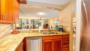 Una cocina con encimeras de granito, armarios de madera y pileta de acero inoxidable, además de una cafetera.