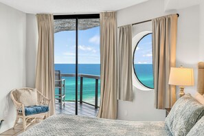 Una camera d'albergo con balcone, un letto, una sedia e vista sull'oceano.