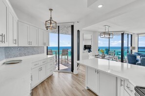 A modern kitchen with white cabinets and a large island, leading to a balcony with a view of the sea. - 2 Free Beach Svc=4 Chairs/2 Umbrellas! Free Beach Bonfires M/F nts! AWESOME View (Miramar Beach)