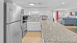 A modern kitchen with stainless steel appliances, a granite countertop, and a view to the living area. - 617- Chic Coastal Retreat - Fully remodeled Beachfront Condo (Destin)