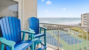 A balcony with two blue Adirondack chairs, a tennis court, and a view of the ocean and beach. - 617- Chic Coastal Retreat - Fully remodeled Beachfront Condo (Destin)