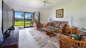 A living room with a large TV, wicker furniture, and a view of the ocean.