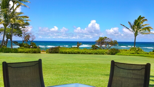 A table with two chairs facing a view of the ocean and palm trees.