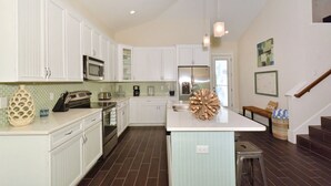 A modern kitchen with white cabinetry, a central island, stainless steel appliances, and a decorative pine cone centerpiece.