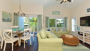 A living room with a dining area, a ceiling fan, a television, and a sign that says "BEACH".