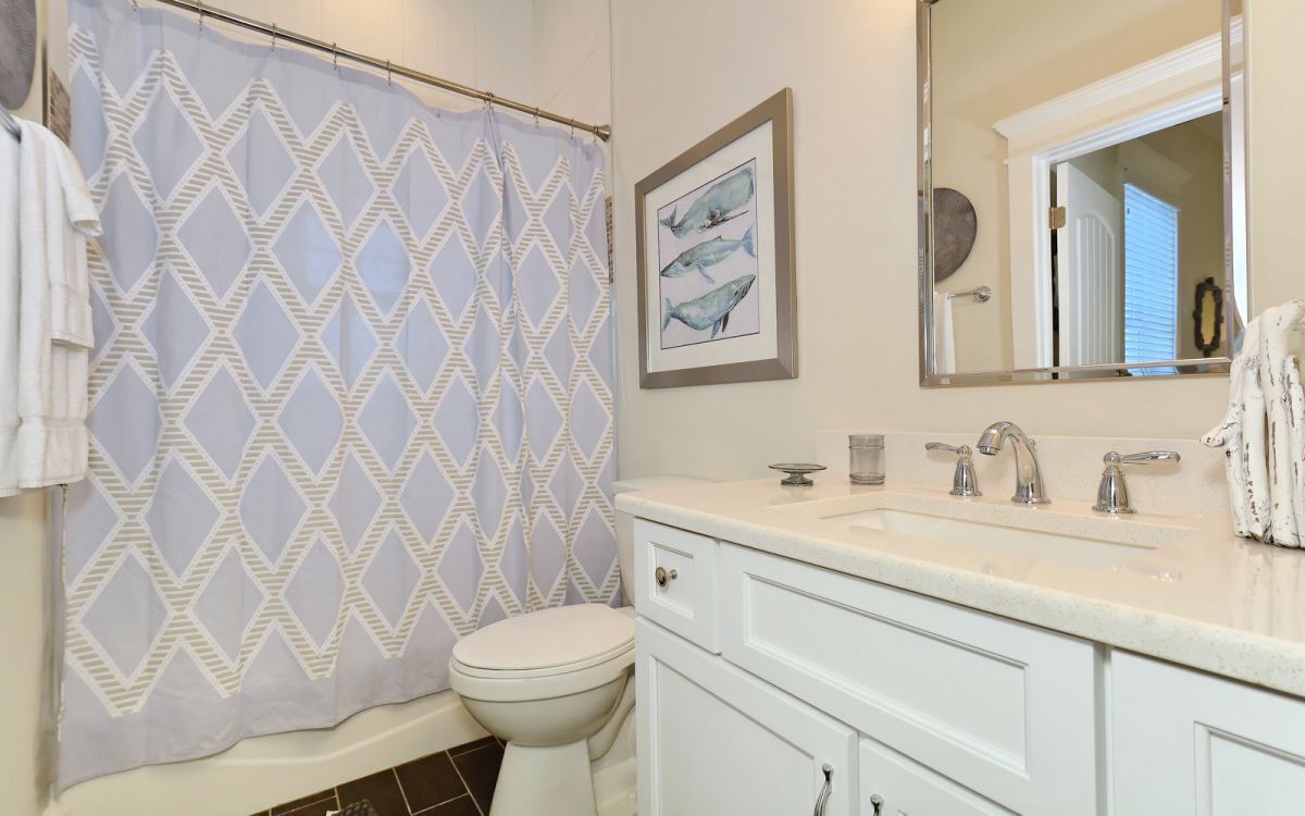 A bathroom with a patterned shower curtain, a toilet, a sink with two faucets, and a framed picture of fish on the wall.