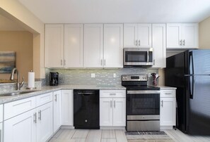 A modern kitchen with white cabinets, stainless steel appliances, and a tiled backsplash. - Spacious Ocean/Pool View Townhome ~ Beautiful White-Sand Beach! (Saint Augustine)
