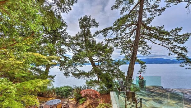 Une terrasse avec une table ronde et des chaises, offrant une vue sur un plan d’eau et des montagnes.