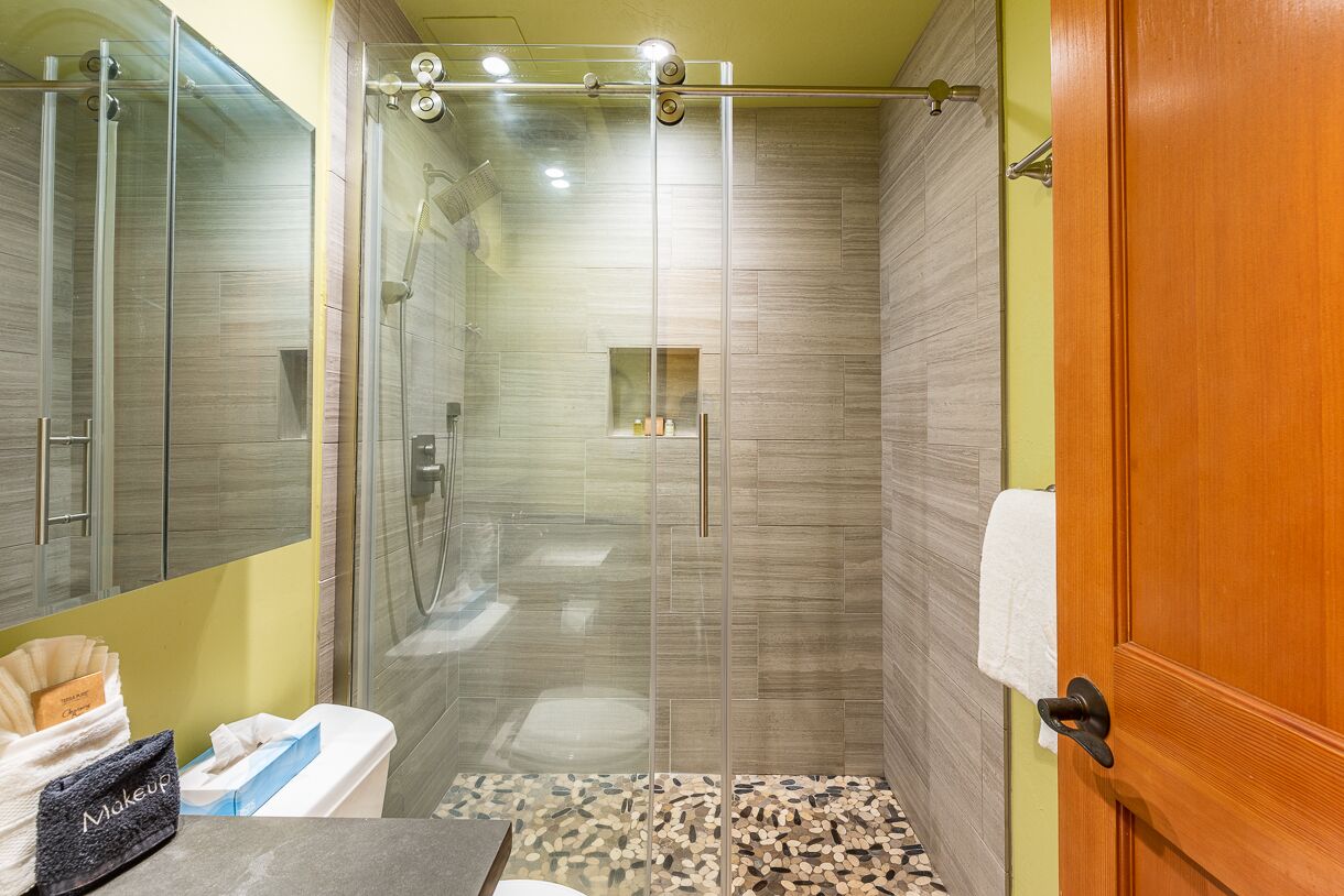 A bathroom with a glass shower enclosure, a toilet, and a sink.